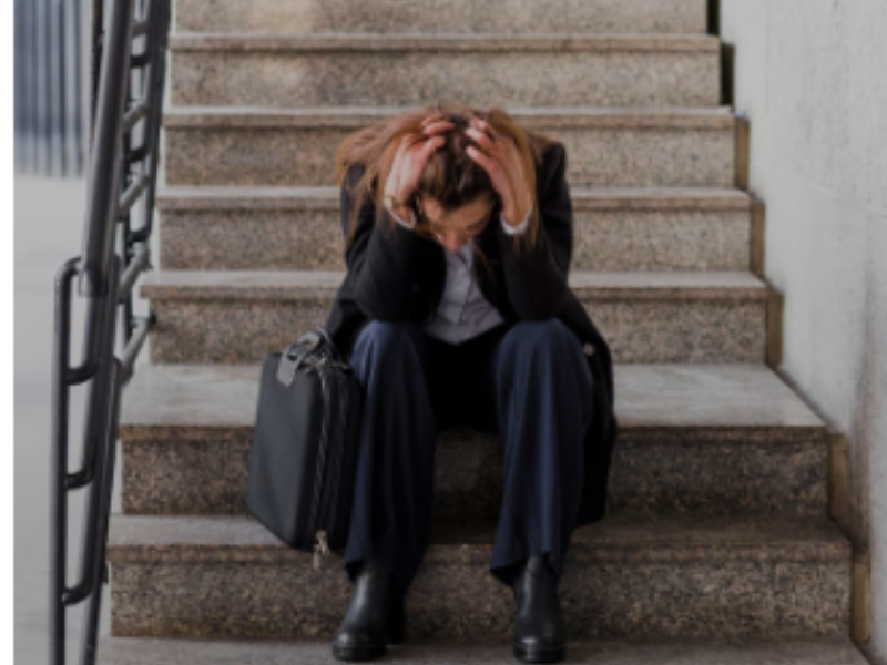 mujer en traje chaqueta sentada en las escaleras con la cabeza entre las manos mirando al suelo